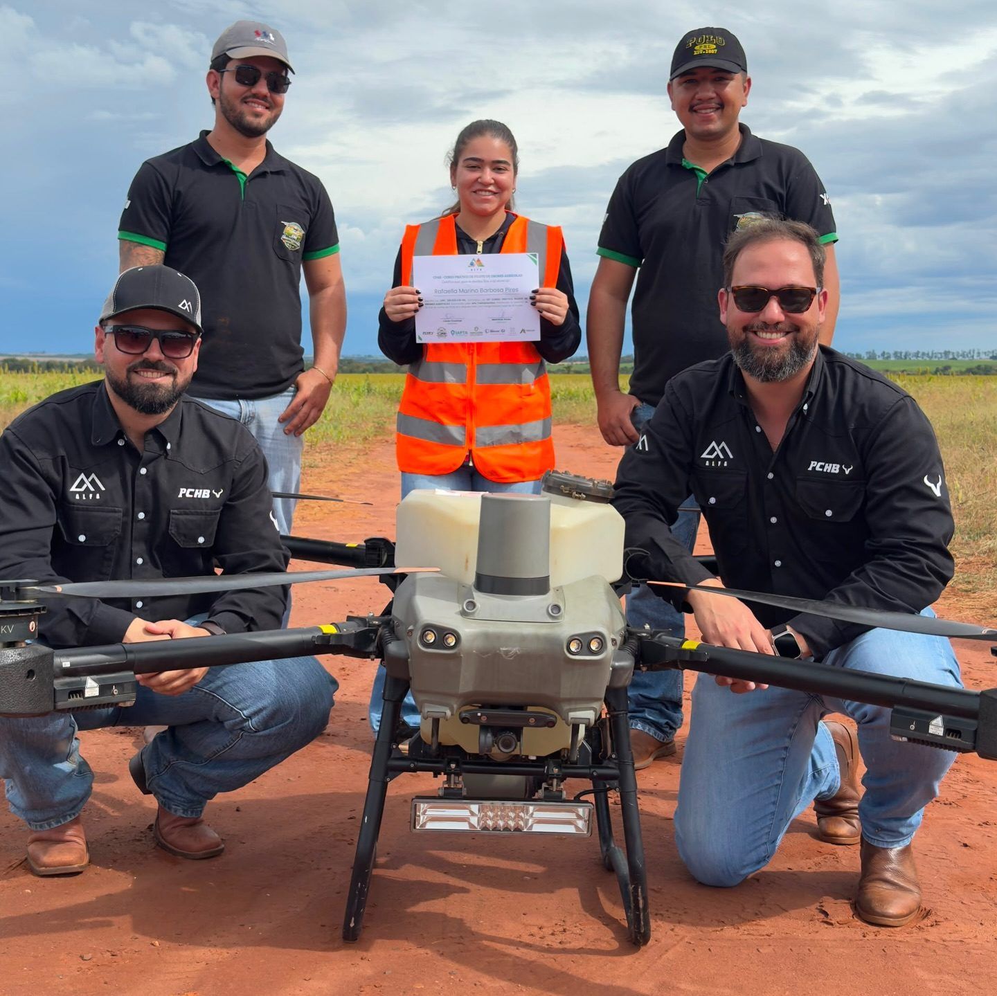Aluna da 13ª turma com o certificado, ao lado dos instrutores e do drone