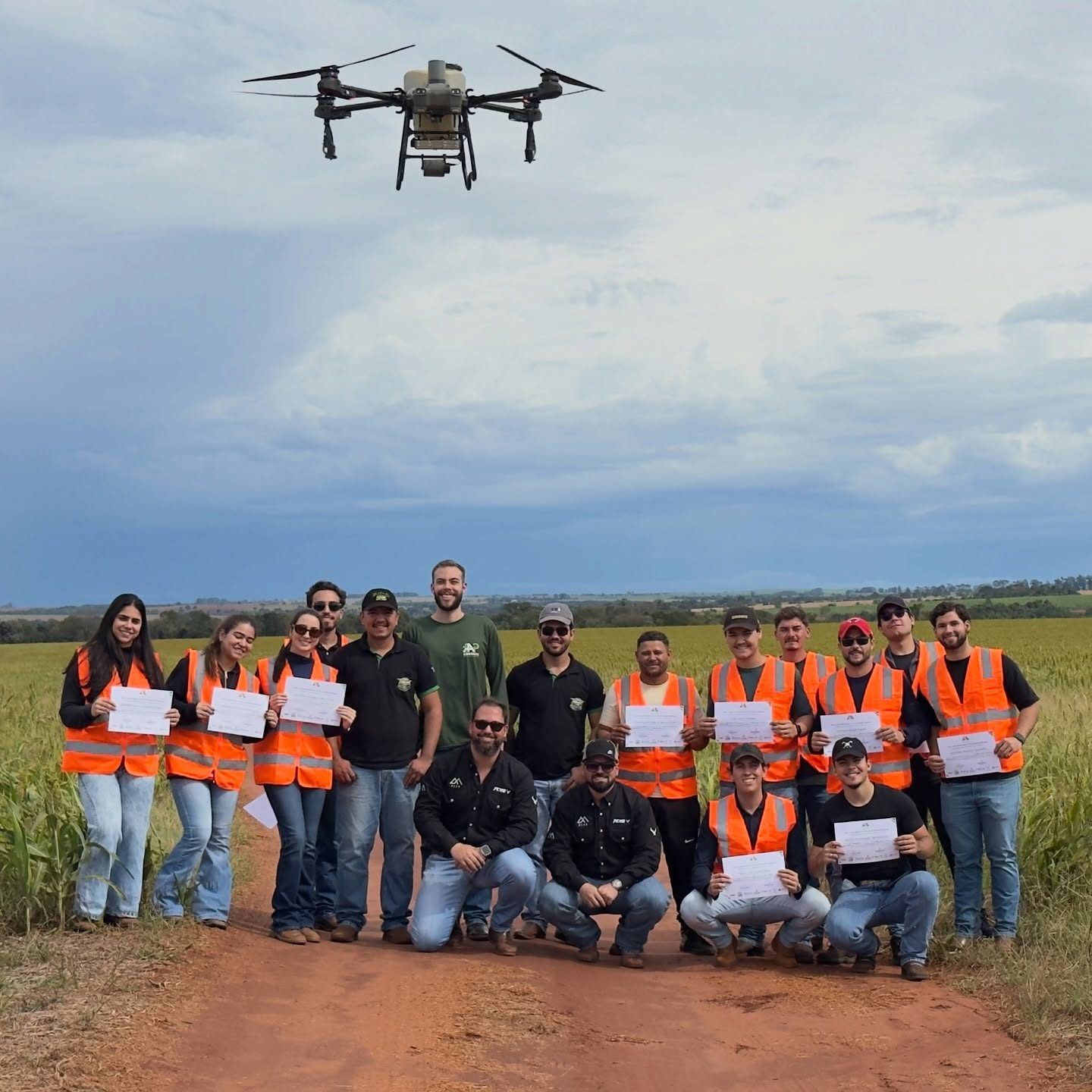 Alunos da 13ª turma com certificados, em campo, com um drone agrícola voando acima