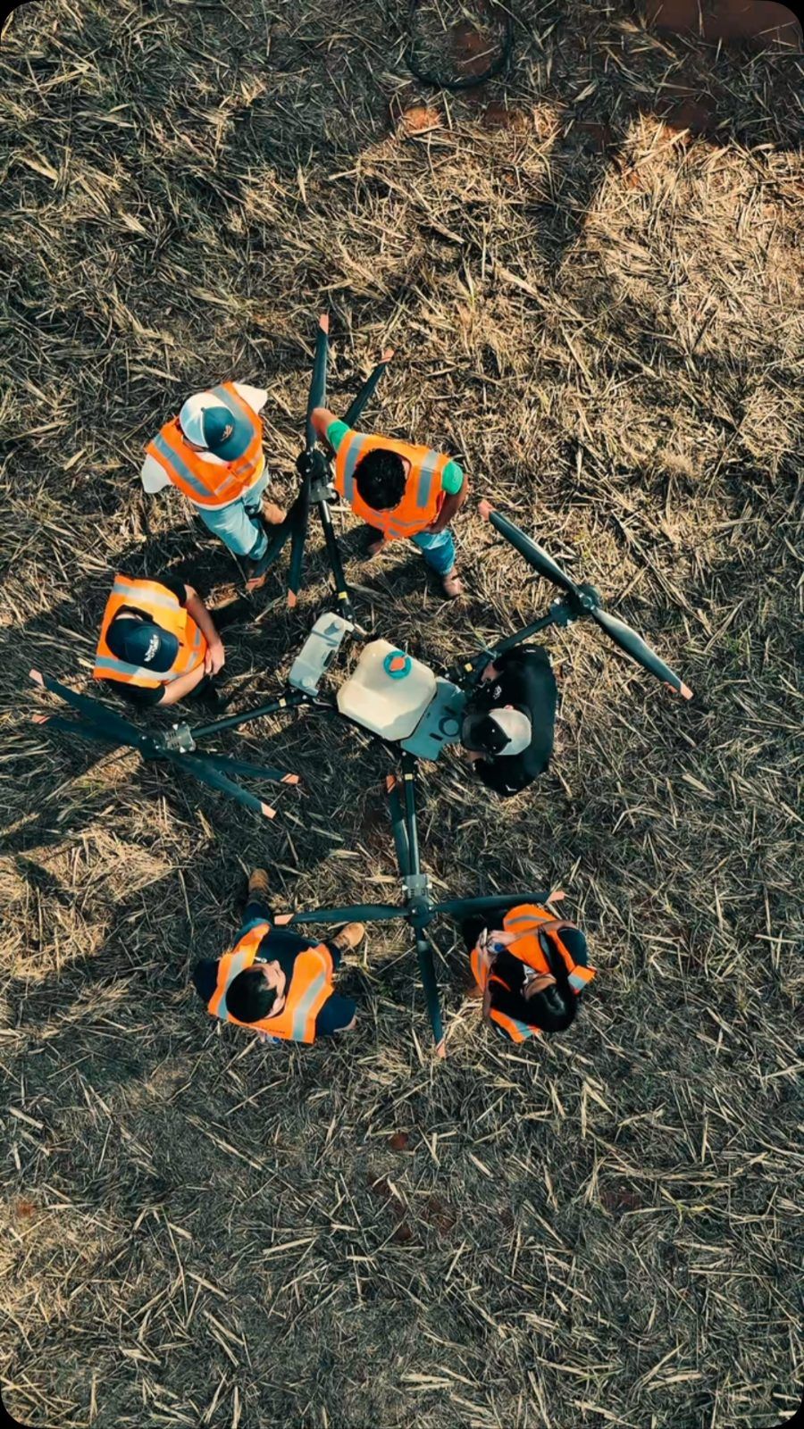 Vista de cima de alunos da Alfa em volta de drones agrícolas no campo